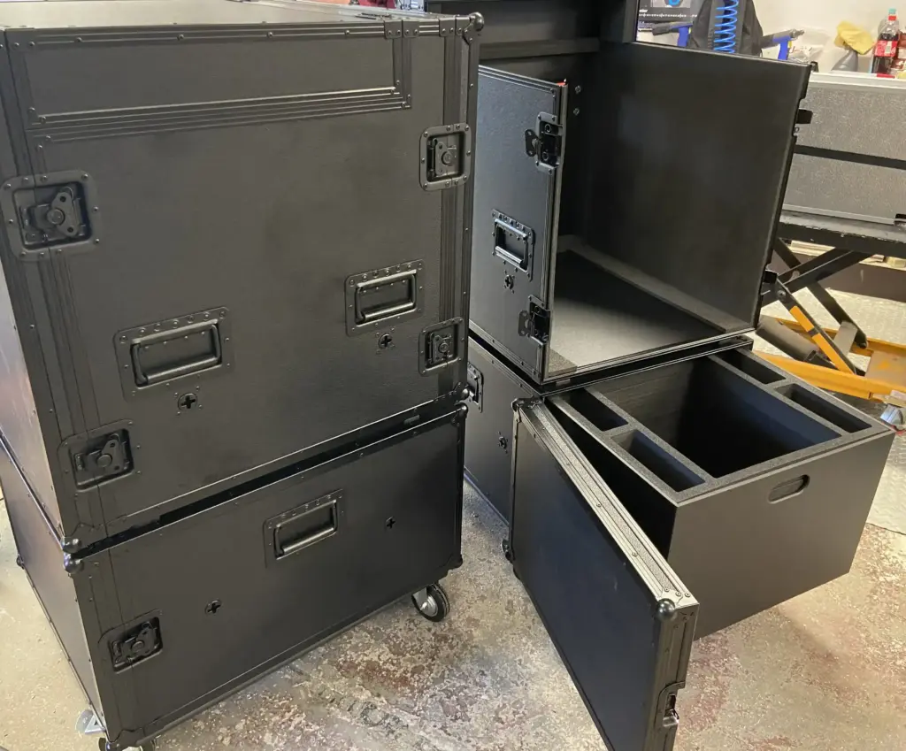 Schwarze Flightcases auf Rollen, zwei mit geöffneter Fronttür, eines mit Schaumstoffeinsatz